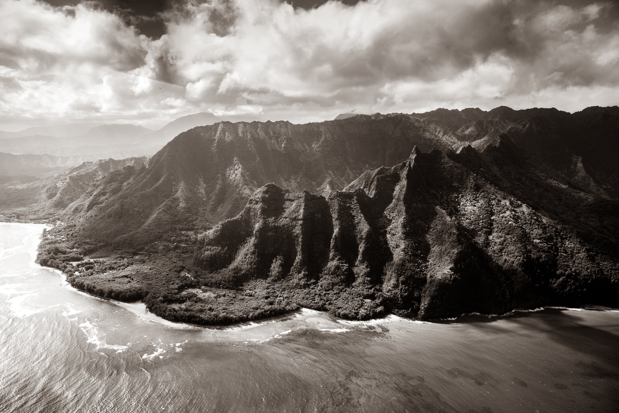 A dramatic sepia-toned aerial landscape photograph of steep rocky mountains meeting the ocean under a cloudy sky.